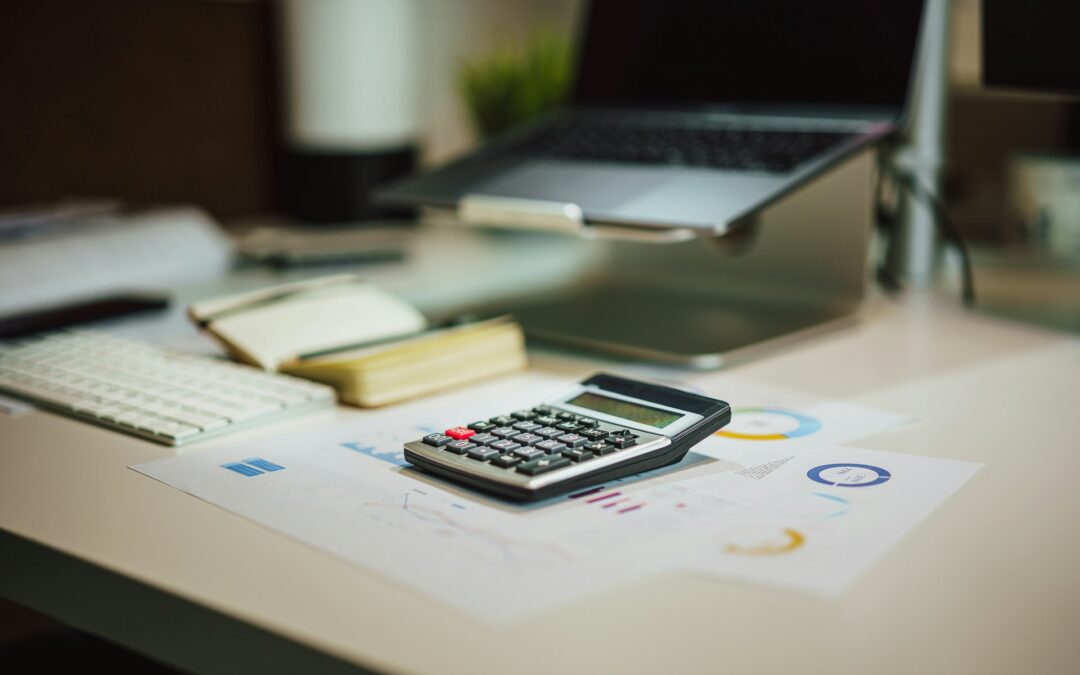 Calculator, laptop and notebook on a desk used to run payroll